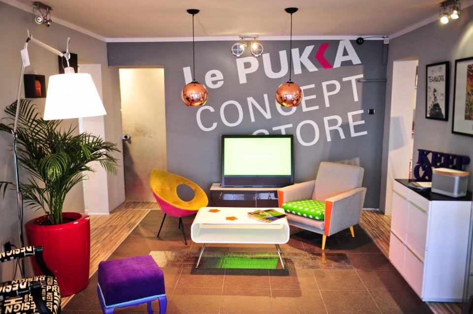 Kolorowe wnętrze z napisem na ścianie Le Pukka Concept Store i kolorowymi fotelami