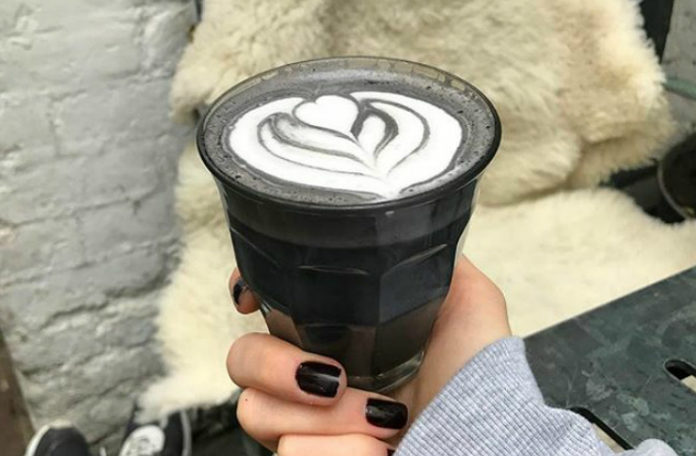 Dłoń z pomalowanymi na czarno paznokciami trzyma w szklankę z czarną kawą