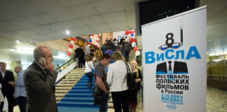 Ludzie stojący w pomieszczeniu, na pierwszym planie plakat Festiwalu Filmowego Wisła