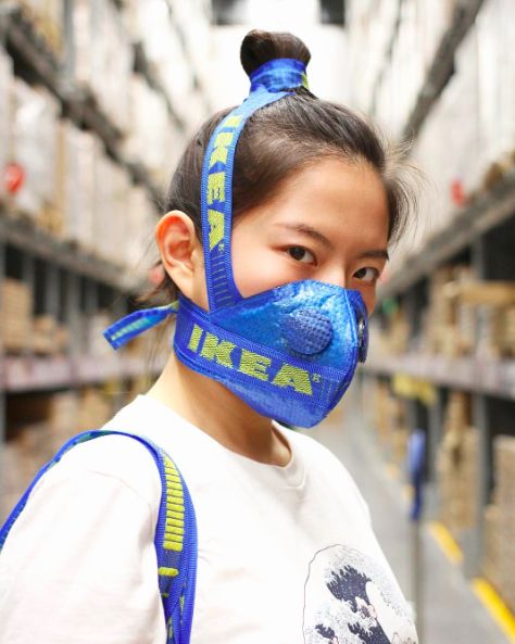 Azjatka stojaca w sklepie, ujecie portretowe boczne, na ustach ma zalozona niebieska maske ktora zakrywa jej kok z brazowych wlosow takze