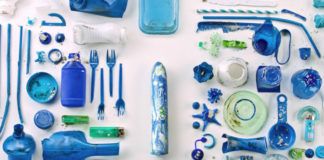 Fotografia reklamowa. Na białym tle poukładane są równo, niebieskie śmieci, takie jak plastikowe widelce, słomki, butelki itp. Na środku widać biało niebieskie dildo.