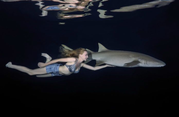 Dziewczyna w szortach i biustonoszu pływa obok rekina