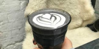 Dłoń z pomalowanymi na czarno paznokciami trzyma w szklankę z czarną kawą