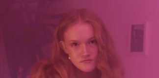 Zdjecie portret dziewczyny z szopa na glowie wszystko jest rozowe w tle widac sciane z obrazem i roslinke