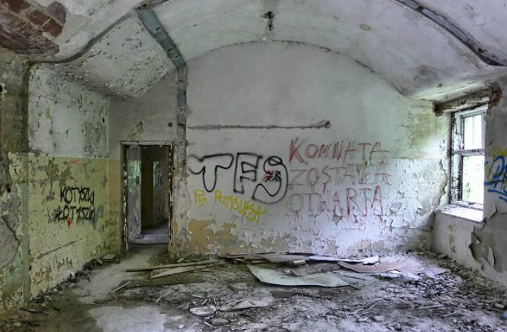 Jedno z pomieszczen w opuszczonych szpitalu w Otwocku. Widac porozbijane szklo, pomazane sciany oraz przejscie do innego pokoju