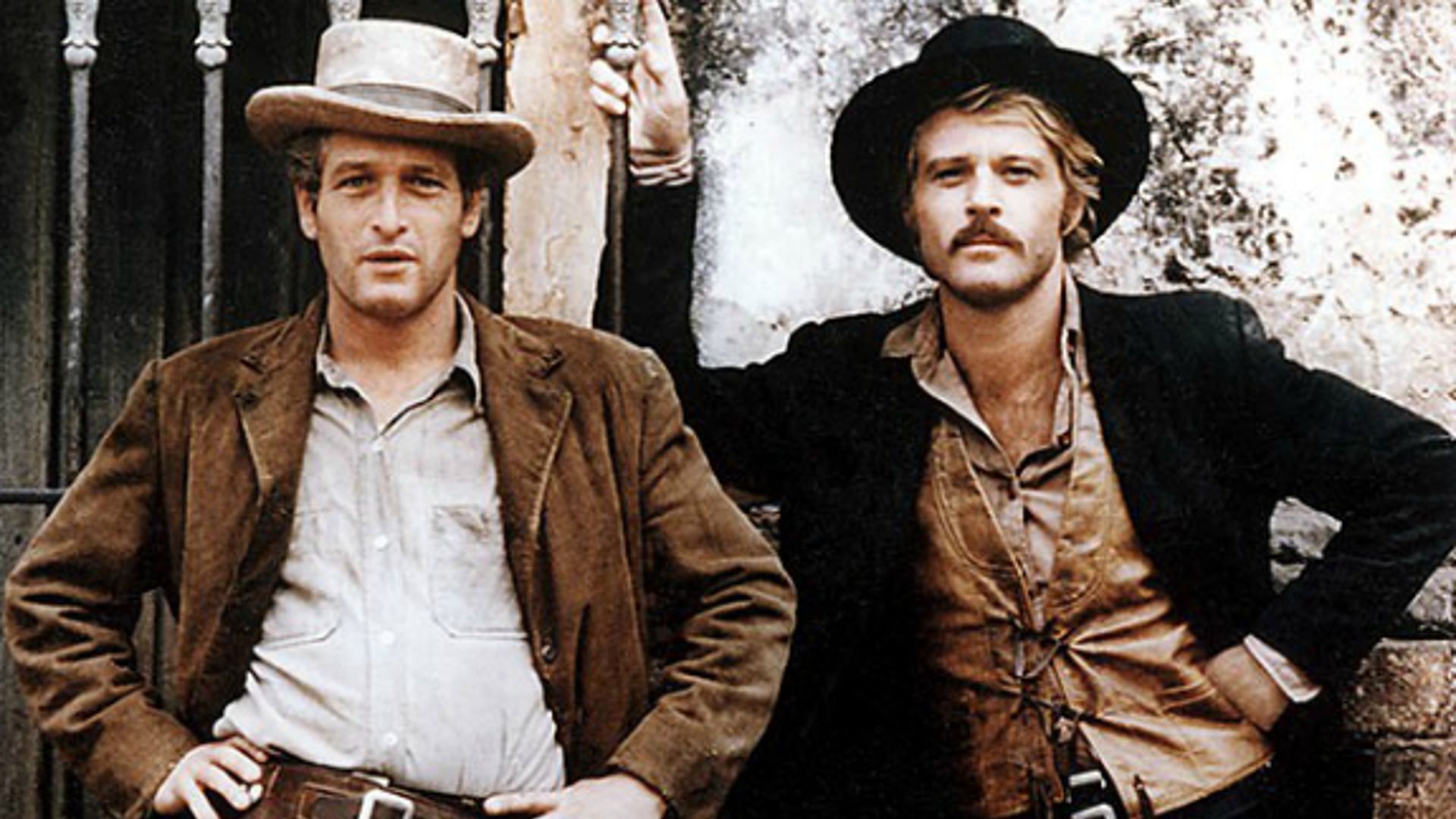 KAdr z filmu " Butch Cassidy and Sundance Kid". Widać dwóch rewolwerowców. Jeden z nich jest w brązowej marynarce i jasnej koszuli. Drugi nosi brązową koszulę i czarną marynarkę. Obydwaj stoją. Ich cechą wspólną jest kapelusz na głowie.