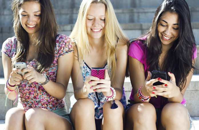 na zdjęciu są trzy dziewczyny wpatrzone w swoje telefony komórkowe