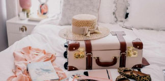 na zdjęciu jest walizka która leży na łóżku, obok walizki są poskładane ubrania oraz buty i kapelusz