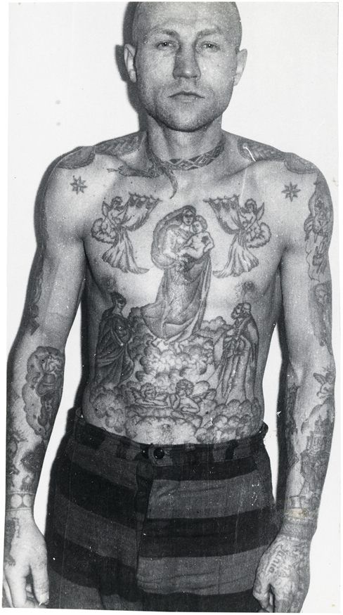 Fotografia wieźnia, który jest widoczny od pasa w górę. Na jego gołej klatce piersiowej jest dużo tatuaży. W okół szyi wytuatuowany jest wąż
