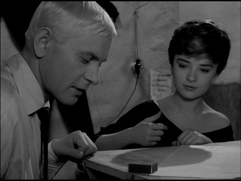 Kadr z filmu " Niewinni Czarodzieje". Przedstawia dwójke bohaterów, mezczyzne i kobiete, ktorzy siedza przy stole i bawią się paczką zapałek.