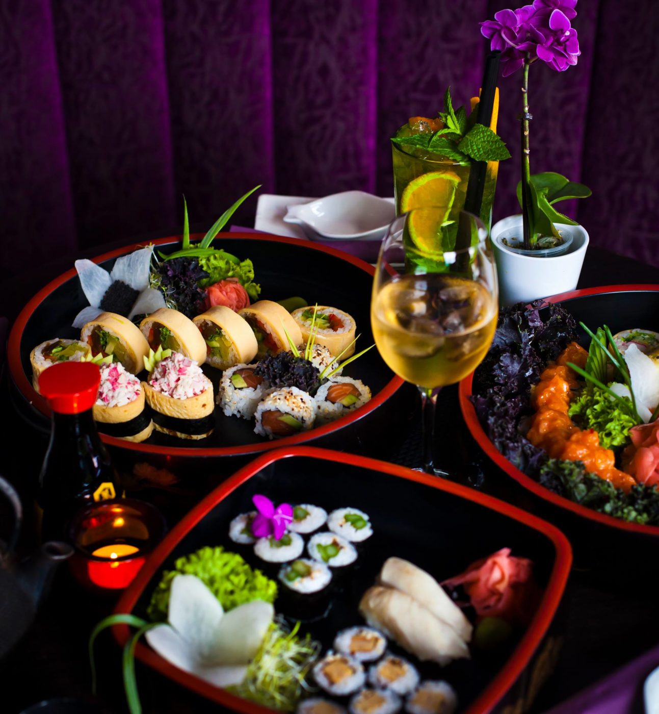Sushi rozłożone na kilku talerzach, w tle fioletowa zasłona