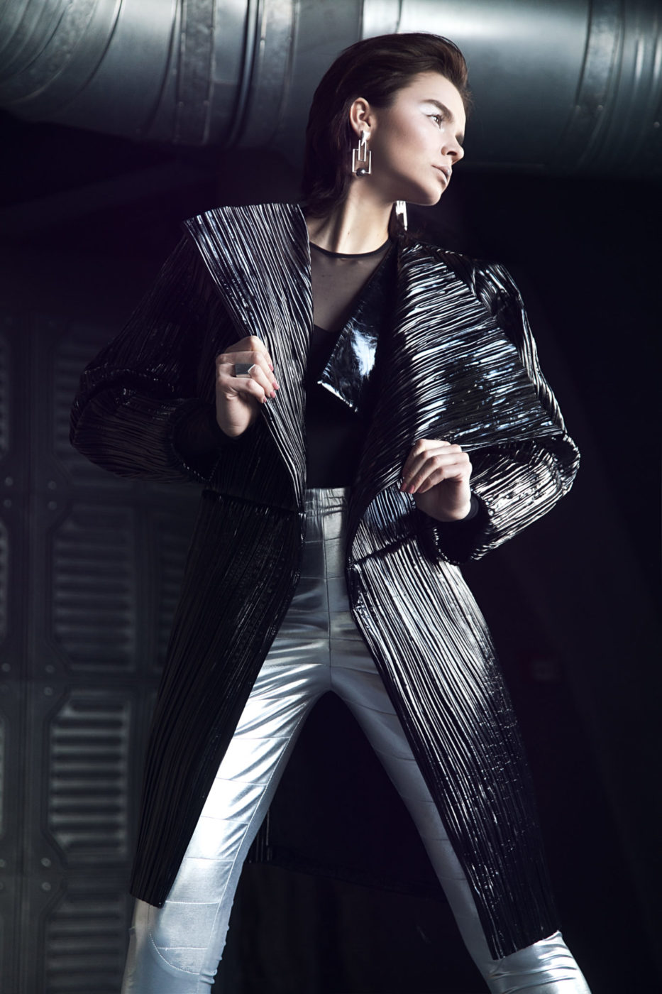 Kobieta stojąca w jasnych spodniach i ciemnym, futurystycznym płaszczu