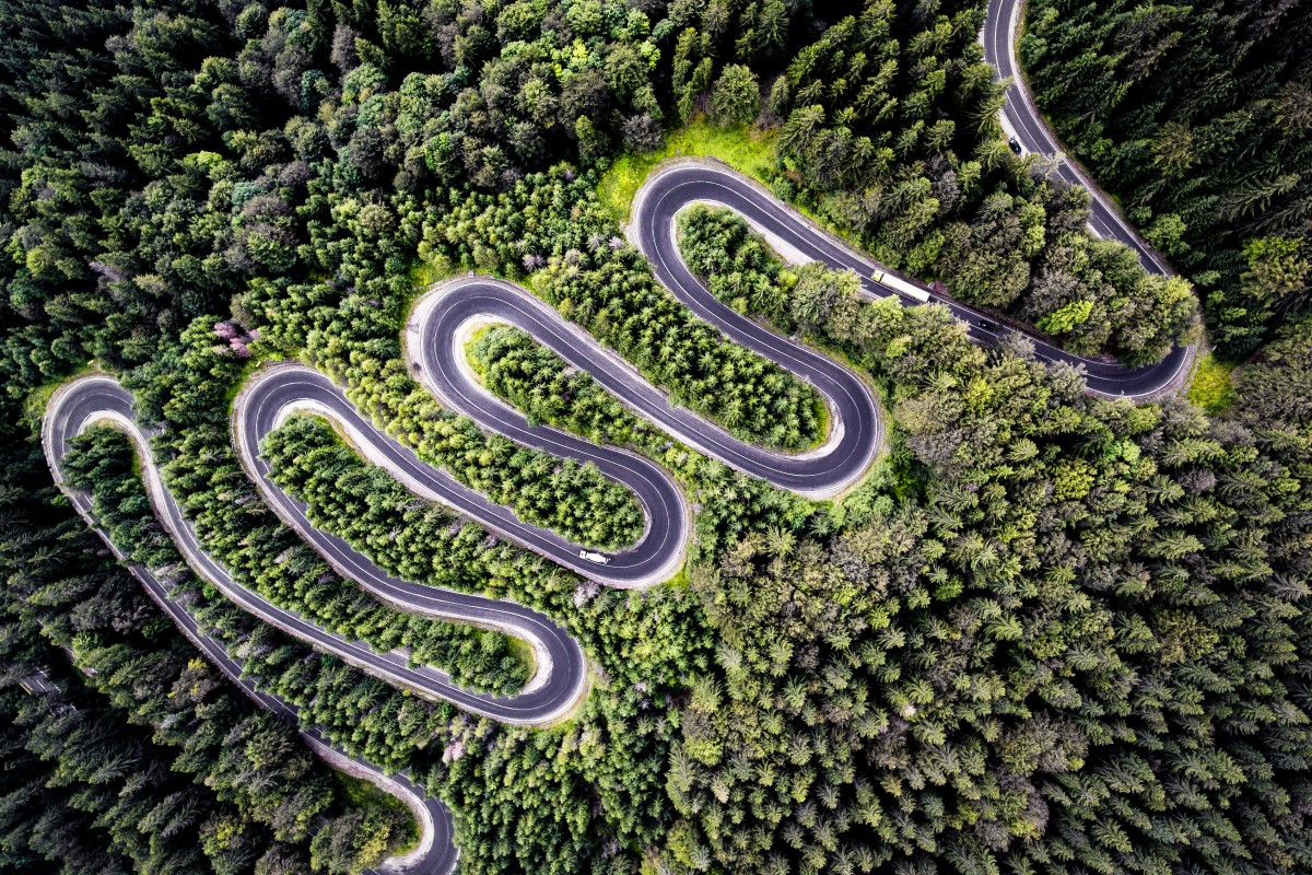 Zdjecie z lotu ptaka przedstawiajaca wijącą się jak wąż drogę asfaltową, która prowadzi to Transylwanii i bardzo kontrastuje wśród otaczającego ją lasu.