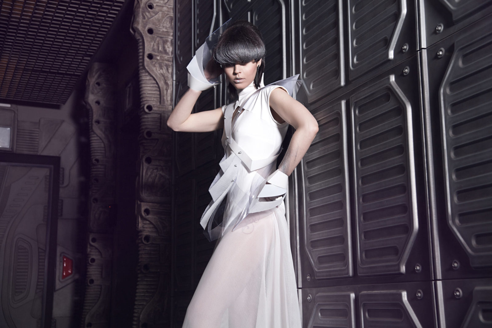 Kobieta ubrana w białą sukienkę z futurystycznymi elementami z fryzurą zakrywającą oczy
