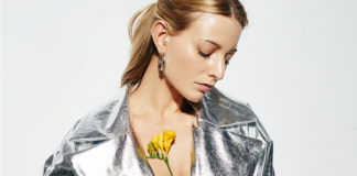 Blondynka z głową skierowaną w dół, z zamknietymi oczami, ubrana w srebrną kurtkę z kwiatami przyczepionymi do klatki piersiowej