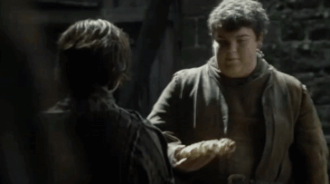 Kadr z serialu Gra o Tron, mężczyzna podaje kobiecie chleb w kszatłcie wilka