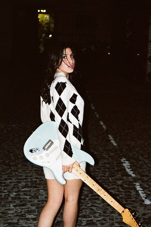 Dziewczyna w sukience w romby, stojąca na ulicy z miętowo-białą gitarą