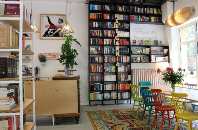 Wnętrze kawiarnii z dużym regałem z książkami i stołem z kolorowymi krzesłami