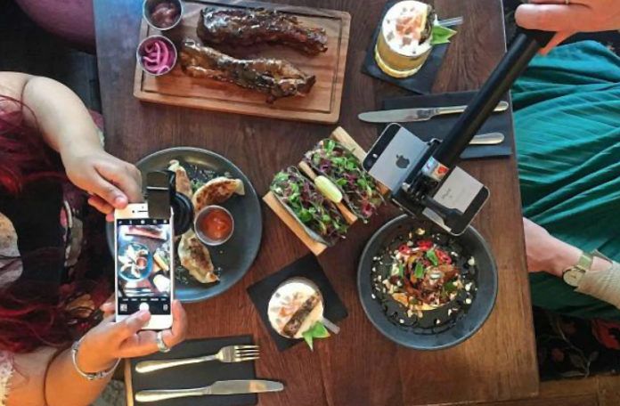 Zdjęcie stołu z góry, kobieta trzymająca smartfon i mężczyzna z selfie stickiem robią zdjęcie posiłku