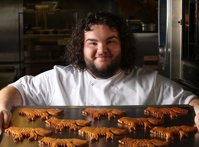Uśmiechnięty mężczyzna kucający przed blachą z wypieczonymi ciastkami w kształcie wilków