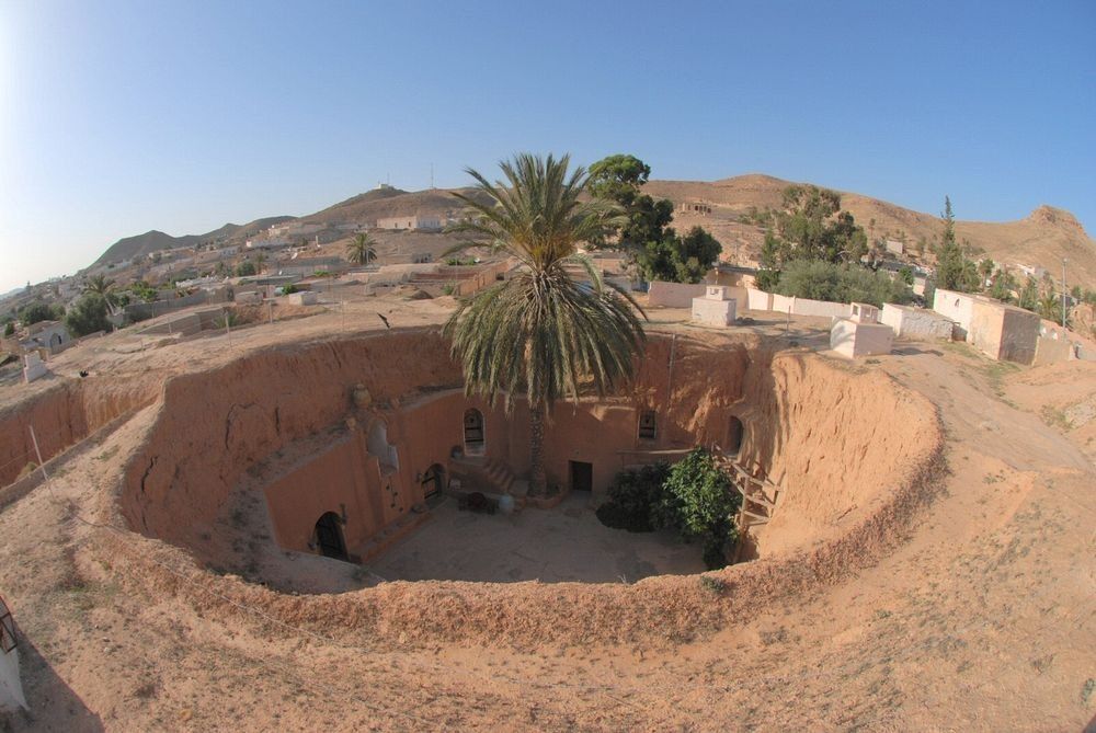 Na zdjęciu jest wioska Tunezyjska. W centralnym punkcie jest okrągły dziedziniec. W ścianach widać wydrążone tunele prowadzące do izb tubylcow