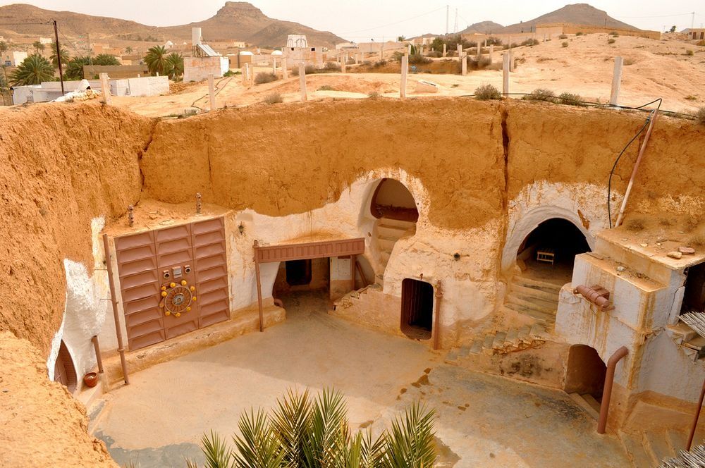 Zdjęcie tunezyjskiego miasteczka, ktore jest wydrążone w piaskowcu. Widać na środku dziedziniec i kilka różnych wejść do tuneli. Podobne osady mają bardzo dobre wlasciwosci izotermiczne. Latem pod ziemią jest chlodniej, a zimą daje ciepło.