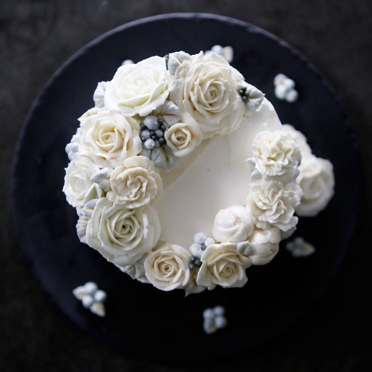 Biały tort leżący na ciemnym stole udekorowany realistyczne wyglądającymi kwiatami