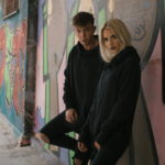 Chłopak i dziewczyna ubrani na czarno, opierający się o ścianę z graffiti