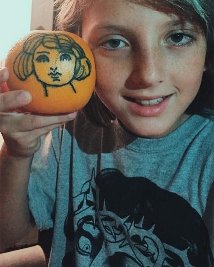 Zdjęcie chłopca trzymającego w dłoni pomarańcz z wytatuowaną twarzą kobiety