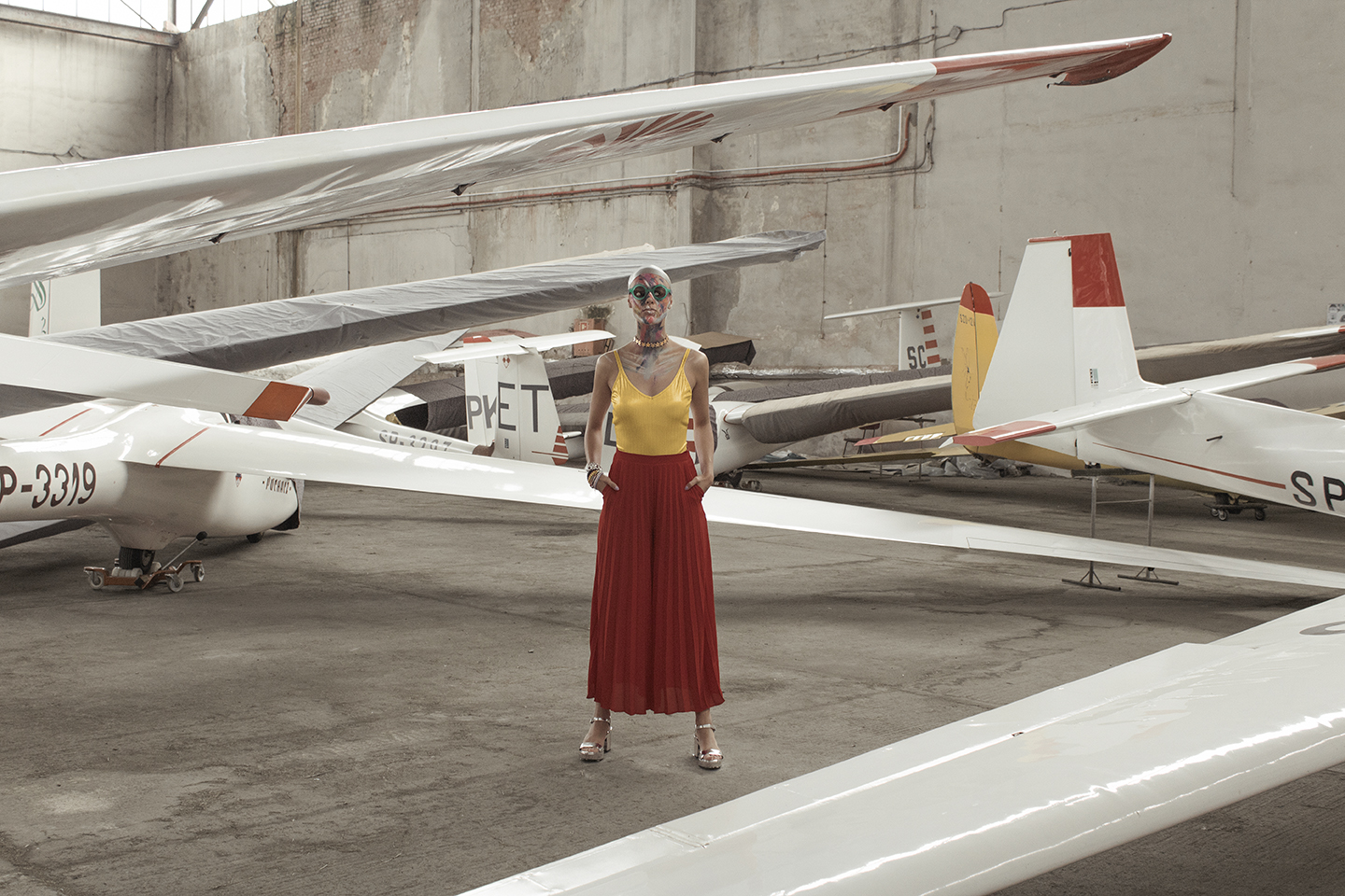 Kobieta ubrana w czerwoną spódnicę i żółtą bluzkę stojąca w otoczeniu samolotów