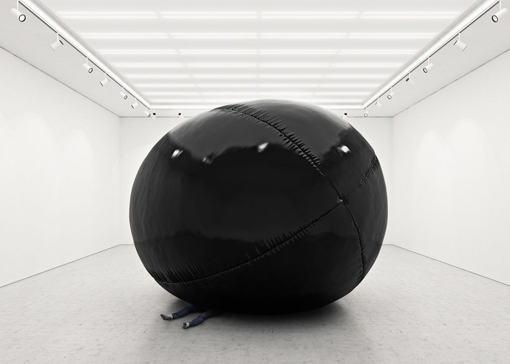 Duży czarny balon w białym pomieszczeniu, który przygniata człowieka.