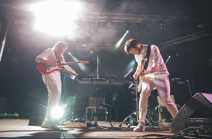 Kobieta i mężczyzna stojący na scenie grający na gitarach, ubrani na biało