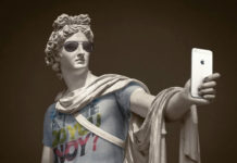 Klasyczna rzeźba ubrana w koszulkę, szalik, okulary, trzymająca w ręku iPhone'a