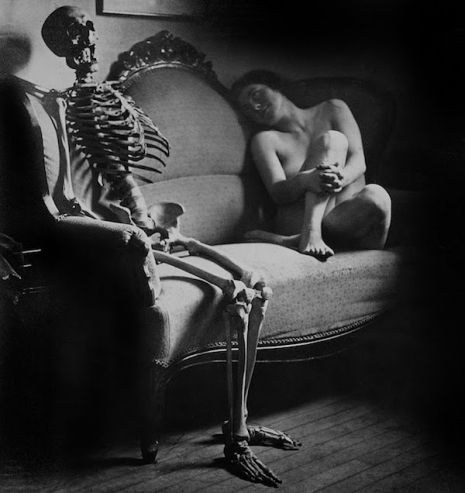 Naga kobieta siedząca a kanapie obok szkieletu