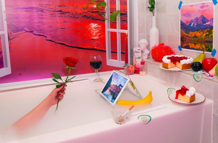 Surrealistyczne zdjęcie z wanną z widokiem na plażę, tabletem, dłonią trzymająca różę, ciastem, winem, papierosem