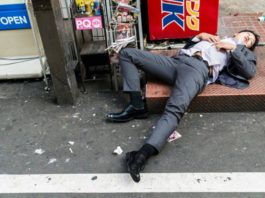 pijany japończyk śpiący okrakiem w garniturze na ulucy Tokio