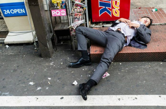 pijany japończyk śpiący okrakiem w garniturze na ulucy Tokio