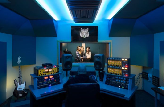 Studio muzyczne z niebieskmi światłami, za szybą trzy wokalistki