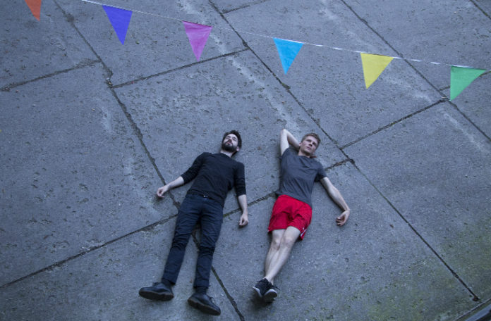 Dwóch chłopaków leżących na chodniku, nad nimi girlanda z chorągiewek