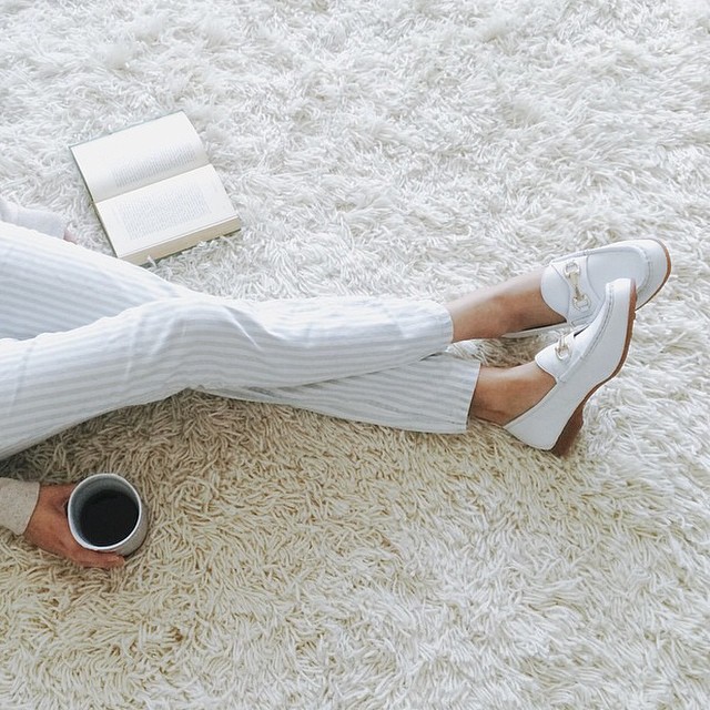 Dziewczyna ubrana w białe spodnie, siedząca na białyym dywanie z kubkiem kawy