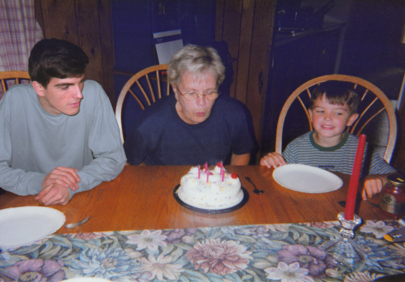 Mężczyzna i chłopiec, a między nimi babcia zdmuchująca świeczki z tortu