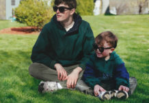 Chłopiec i mężczyzna siedzą w zielonych bluzach i okularach na trawie