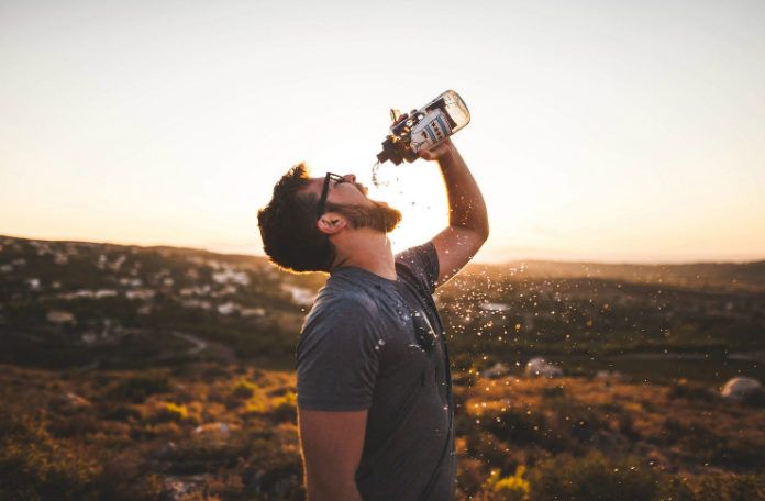 Mężczyzna na pustyni pijący z butelki jakiś trunek, w tle rozciąga się pustynia