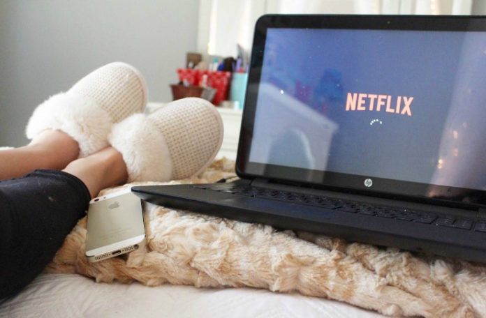 Laptop z włączonym Netflixem, kobiece nogi i telefon