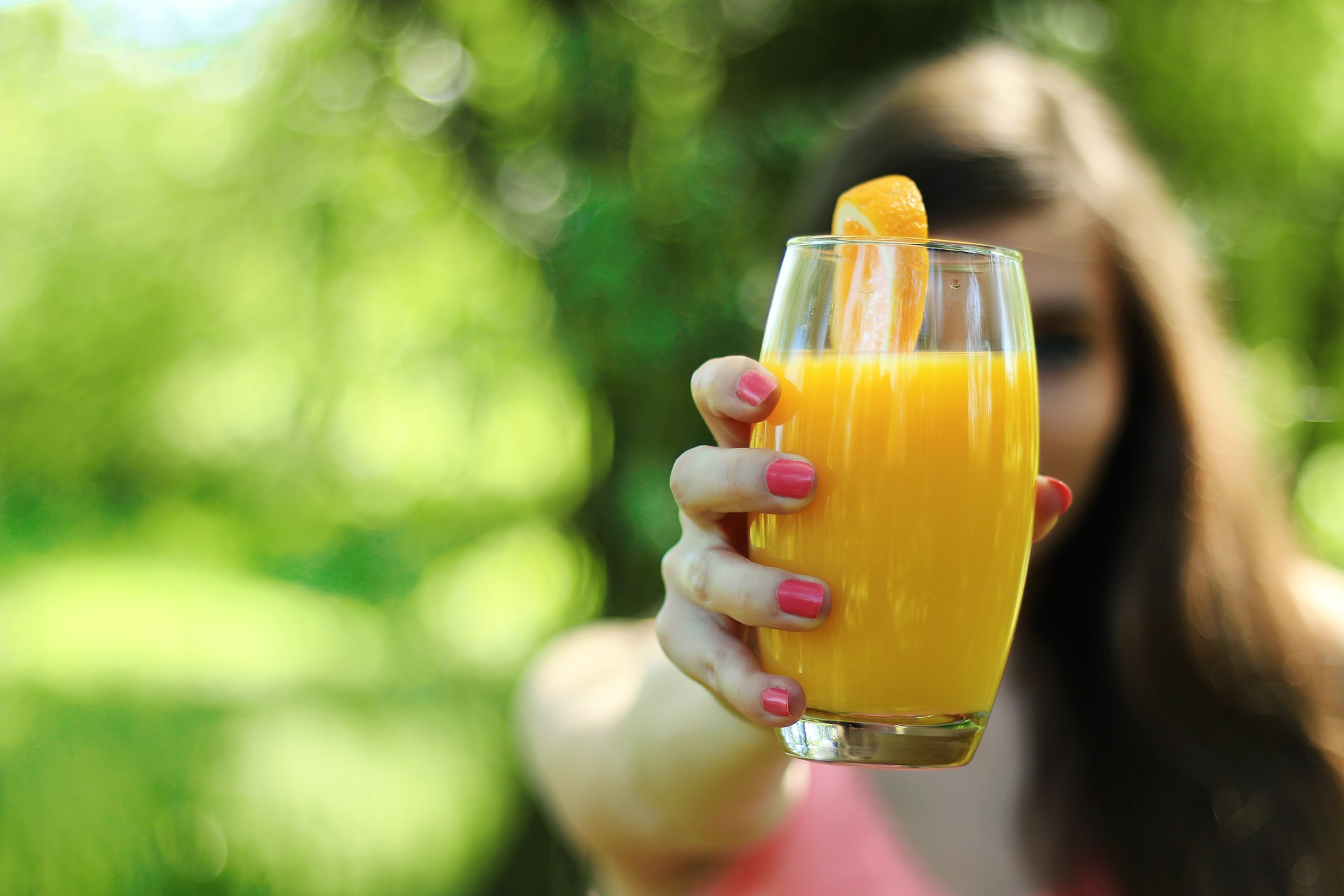 Kobieta trzymająća w wyprostowanej ręce przed sobą szklankę soku pomarańczowego