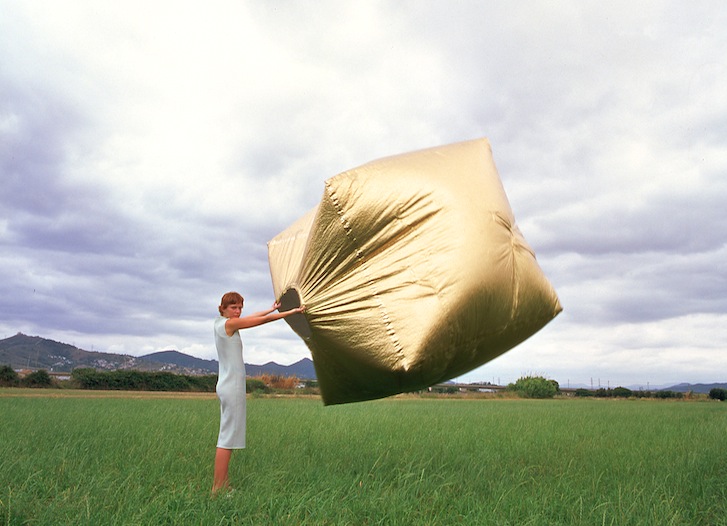Kobieta trzymająca w powietrzu dużą, złotą kostkę wypełnioną powietrzem
