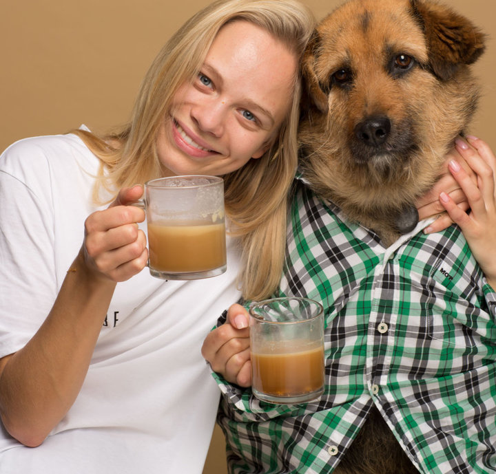 Kobieta trzymająca kawę przytula się do psa.