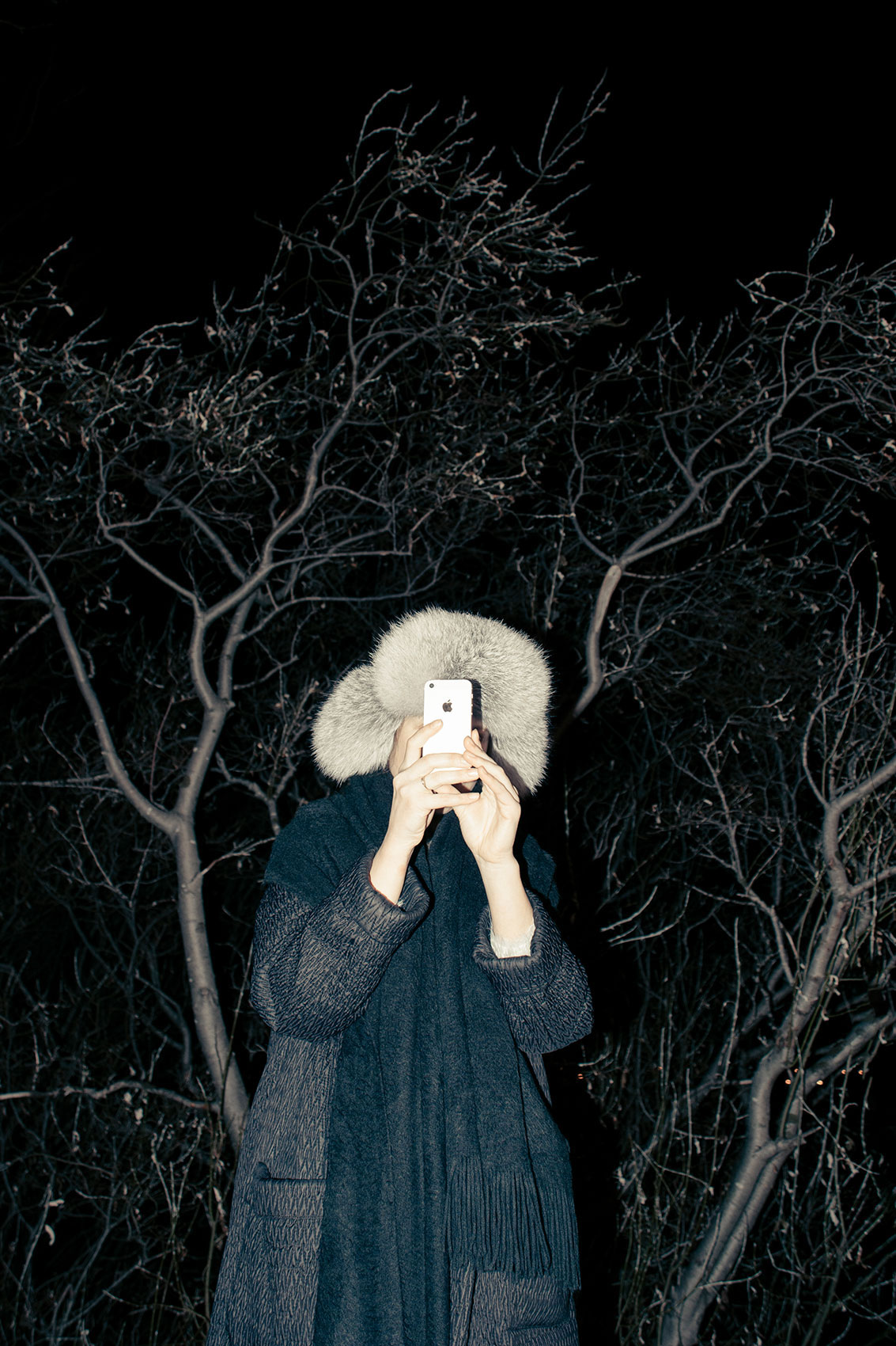 Kobieta w ciemnościach trzyma telefon przy twarzy.