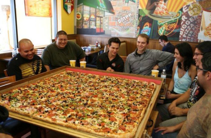 Wielka pizza i ludzie siedzący dookoła niej