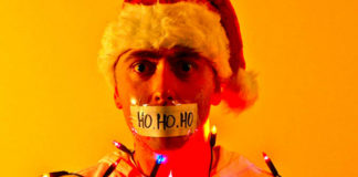 Mężczyzna w czapce Mikołaja z zaklejonymi ustami i obwiązany świątecznymi lampkami